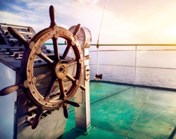 Mit einer Charterversicherung segeln Sie sicher Holz-Steuerrad in der Abendsonne